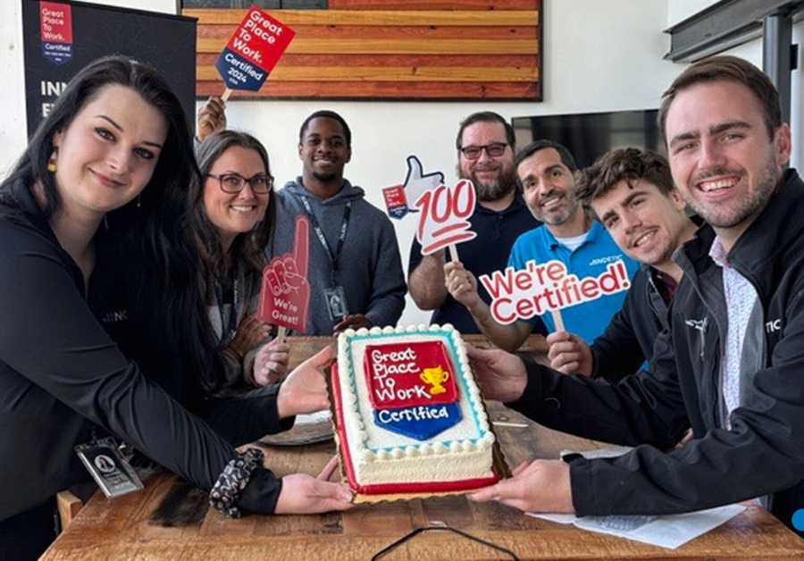  A group of eight smiling employees proudly hold a cake with a 